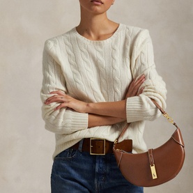 Model carrying Polo Ralph Lauren Cuoio shoulder bag with gold-tone hardware, styled with cream cable-knit sweater and blue jeans.