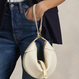 Model carrying Polo Ralph Lauren ivory shoulder bag with gold-tone hardware and short top handle, styled with dark denim jeans and navy blazer