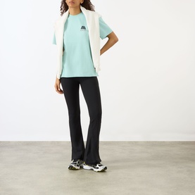 Model wearing Adanola Logo Graphic Oversized T-Shirt in Ocean Blue, styled with a cream gilet, black flared trousers and chunky trainers.