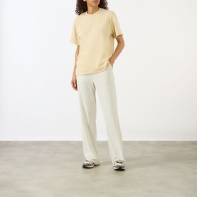 Model wearing Adanola Logo Graphic Oversized T-Shirt in Caramel Beige with cream wide-leg trousers and grey trainers.