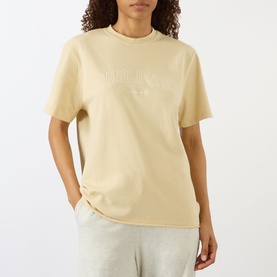 Model wearing Adanola Logo Graphic Oversized T-Shirt in Caramel Beige with embossed logo, round neck, styled with grey joggers.