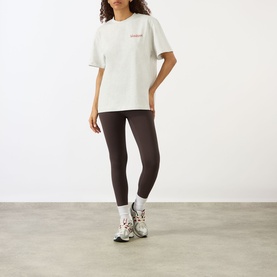 Model wearing Adanola Logo Graphic Oversized T-Shirt in Light Grey Melange with dark leggings and white chunky trainers.