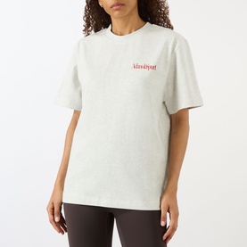 Model wearing Adanola Logo Graphic Oversized T-Shirt in Light Grey Melange with red chest logo, styled with dark brown leggings.