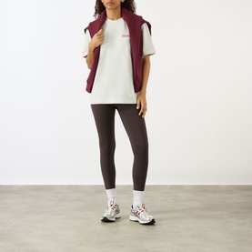 Model wearing Adanola Logo Graphic Oversized T-Shirt in Light Grey Melange, styled with burgundy gilet, brown leggings and chunky trainers.