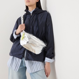 Model carrying Anxious Preoccupied The Oversized Belt Bag in silver and lime green with gold-tone hardware, worn crossbody. Styled with navy jacket