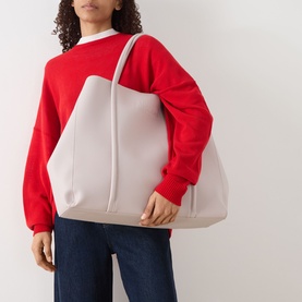 Model carrying Anxious Preoccupied The Oversized Logo Tote Bag in beige, faux grained finish with dual shoulder straps, styled with a red sweatshirt