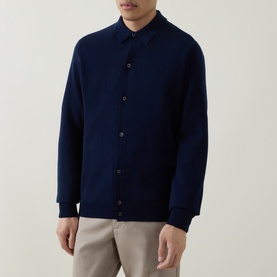 Model wearing Aspesi Knitted Polo Shirt in blue wool, featuring button fastenings, polo collar, and long sleeves, styled with beige trousers.