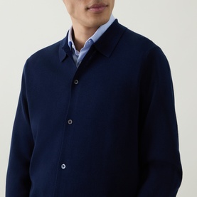 Model wearing Aspesi Blue Knitted Polo Shirt cardigan with button fastenings and polo collar, styled over a light blue shirt.