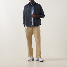 Model wearing Aspesi navy nylon casual jacket, styled with blue shirt, beige trousers and grey trainers.