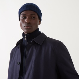 Model with Aspesi Rib-Knit Beanie Hat in Black Blue, turn-up hem, worn with a navy overcoat and black zip-through jacket.