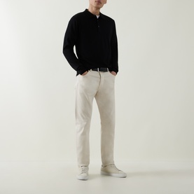Model wearing Aspesi Solid Knitted Polo Shirt in black wool, long sleeves, ribbed trims, styled with cream trousers and white trainers.
