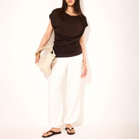Model wearing Mint Velvet Brown Double Layer Drape Top with slash neck, styled with white wide-leg trousers, sandals, and cream tote bag.