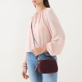 Model carrying Gianni Chiarini Alifa Crossbody Bag in burgundy suede with silver-tone hardware, worn crossbody over pink blouse and jeans