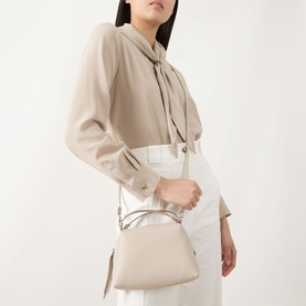 Model carrying Gianni Chiarini Alifa Crossbody Bag in taupe grained leather, silver-tone hardware, worn as crossbody with white trousers and beige