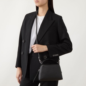 Model carrying Gianni Chiarini Alifa Crossbody Bag in nero grained leather, silver-tone hardware, top handles, worn with black blazer