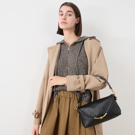 Model carrying Gianni Chiarini Bea Crossbody Bag in black textured leather with gold-tone knotted hardware, styled with beige trench coat and khaki