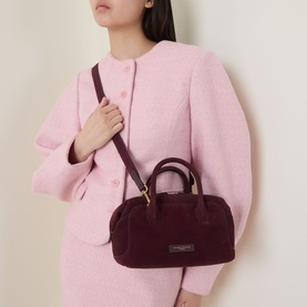Model carrying Gianni Chiarini Gemma Crossbody Bag in burgundy suede with gold-tone hardware and crossbody strap, styled with a pink jacket