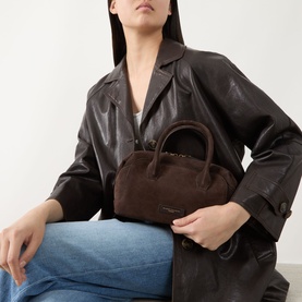 Model carrying Gianni Chiarini Gemma Crossbody Bag in brown suede with gold-tone hardware and top handles, styled with dark leather jacket and blue