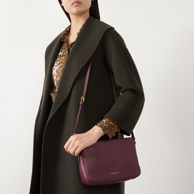 Model carrying Gianni Chiarini Laura Crossbody Bag in antique ruby grained leather with gold-tone hardware and adjustable strap, styled with dark