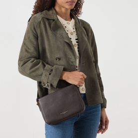 Model carrying Gianni Chiarini Laura Crossbody Bag in brown grained leather with gold-tone hardware and adjustable strap, styled with khaki jacket