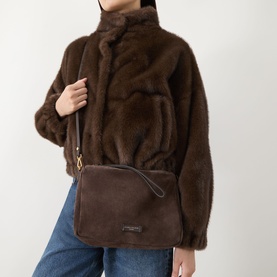 Model carrying Gianni Chiarini Nora Crossbody Bag in Moka suede, gold-tone hardware, worn on crossbody strap, styled with brown faux-fur jacket