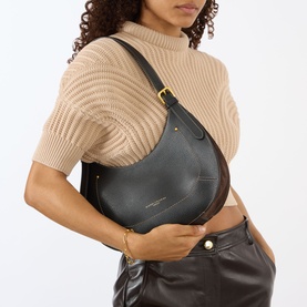 Model carrying Gianni Chiarini Gabry Shoulder Bag in black grained leather with gold-tone hardware, worn over a beige knit top and brown leather