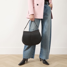 Model carrying Gianni Chiarini Helena Round Shoulder Bag in black grained leather with silver-tone hardware, styled with pink blazer and wide-leg