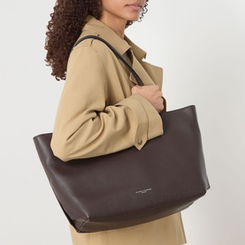 Model carrying Gianni Chiarini Barbara Tote Bag in brown grained leather with silver-tone hardware, styled with a camel coat