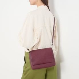 Model carrying Gianni Chiarini Three Flap Leather Crossbody Bag in antique ruby, silver-tone hardware, worn crossbody over cream jacket and green