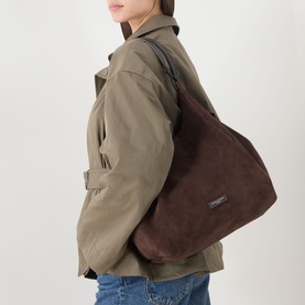 Model carrying Gianni Chiarini Dua Suede Tote Bag in brown, slouchy silhouette with looped handles, worn over shoulder with khaki jacket.