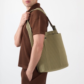 Model carrying a large olive green pleated tote bag with short handles, styled with a matching pleated co-ord set