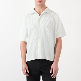 Model wearing Issey Miyake casual shirt in Duomo Green, short-sleeve pleated design with camp collar and button front, styled with black trousers