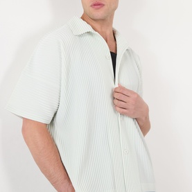Model wearing Issey Miyake casual shirt in Duomo Green with pleated texture, short sleeves, and open collar, styled over a black vest.