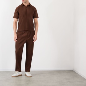 Model wearing Issey Miyake Anchor Brown casual trousers with matching brown polo shirt and white trainers.