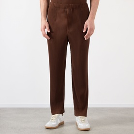 Model wearing Issey Miyake Anchor Brown pleated casual trousers with elasticated waist, styled with white leather trainers.