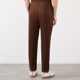 Model wearing Issey Miyake Anchor Brown ribbed pleated casual trousers, styled with white leather trainers, rear view.