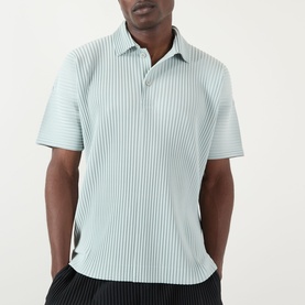 Model wearing Issey Miyake polo in Boboli Moss Ash, featuring fine vertical pleats, short sleeves, and open collar. Styled with black trousers.