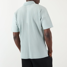 Model wearing Issey Miyake polo in Boboli Moss Ash, short-sleeve pleated texture, rear view, with black trousers.