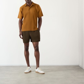Model wearing Issey Miyake Venice Boat Brown polo shirt with olive shorts and white trainers.