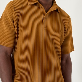 Model wearing Issey Miyake polo in Venice Boat Brown, featuring all-over vertical pleating and short sleeves with open collar.