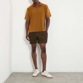 Model wearing Issey Miyake Venice Boat Brown polo shirt with dark olive shorts and white trainers.