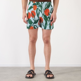 Model wearing Issey Miyake blue printed shorts with orange floral motif, styled with black leather sandals