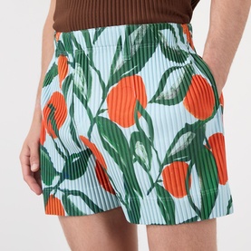 Model wearing Issey Miyake blue pleated shorts with bold orange and green tulip print, styled with a brown top.