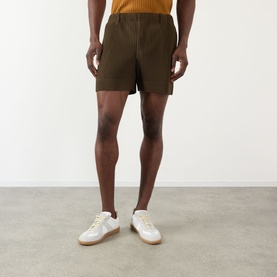 Model wearing Issey Miyake shorts in Genova Metal Ocher, pleated texture, paired with white low-top trainers
