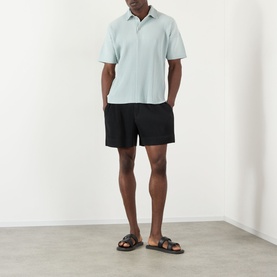 Model wearing Issey Miyake black polyester shorts with a light blue polo shirt and brown leather sandals.