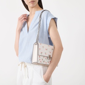 Model carrying Kate Spade Deco Vibrant Buds Crossbody Bag in cream multi with floral embroidery, silver chain strap and K hardware clasp.