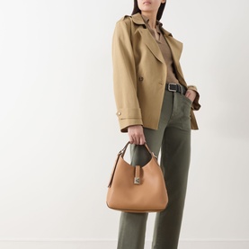 Model carrying Kate Spade Deco Medium Tote Bag in Garden Soil grained leather with gold-tone hardware, styled with camel jacket and olive trousers