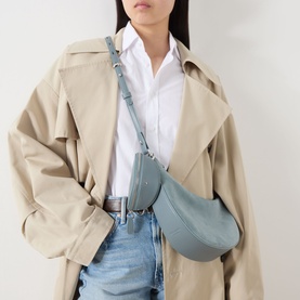 Model carrying Kate Spade Duo Suede Leather Crossbody Bag in Dark English Sea, silver-tone hardware, worn crossbody over white shirt and trench coat