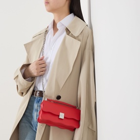 Model carrying Kate Spade Deco Wavy Mini Crossbody Bag in Heirloom Tomato red leather, silver chain strap, styled with trench coat and jeans