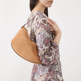 Model carrying Kate Spade Loop Suede Leather Shoulder Bag in Garden Soil, crescent silhouette with silver-tone hardware, worn over shoulder, styled